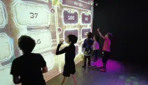 Children in front of an interactive educational wall solving mathematical operations.