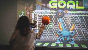 Femme lançant une balle sur un mur interactif représentant un but de football futuriste.