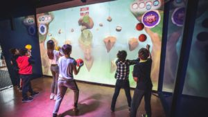 Enfants jouant ensemble à un jeu d’aventure sur mur interactif, lançant des balles dans une arène immersive