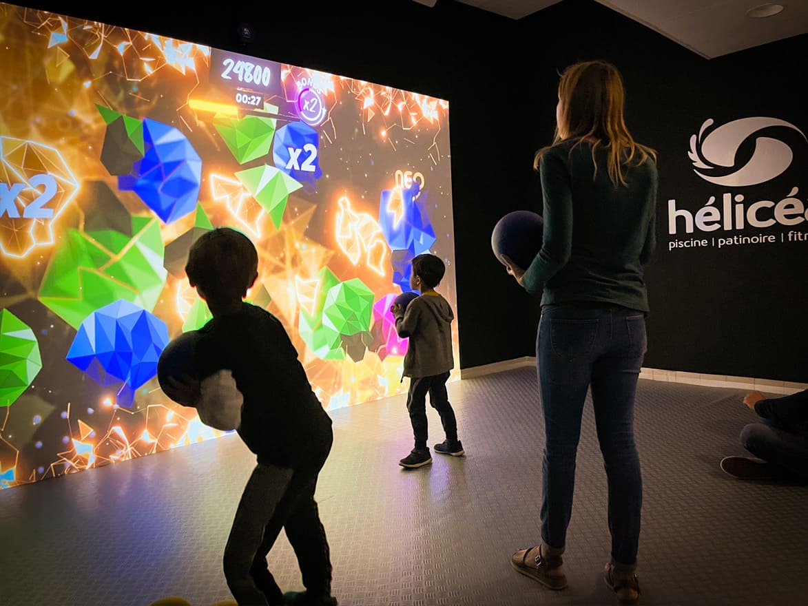Famille jouant à Meteor of Colors sur un mur interactif Neo One dans l'espace Hélicea