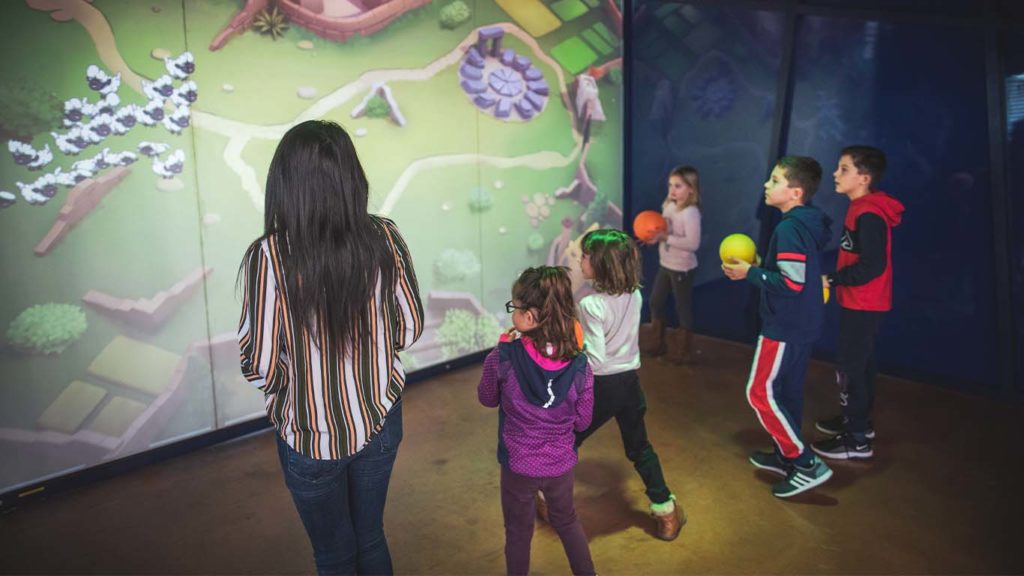 Un groupe d’enfants joue ensemble à un jeu d’adresse projeté sur un mur interactif dans un espace immersif.