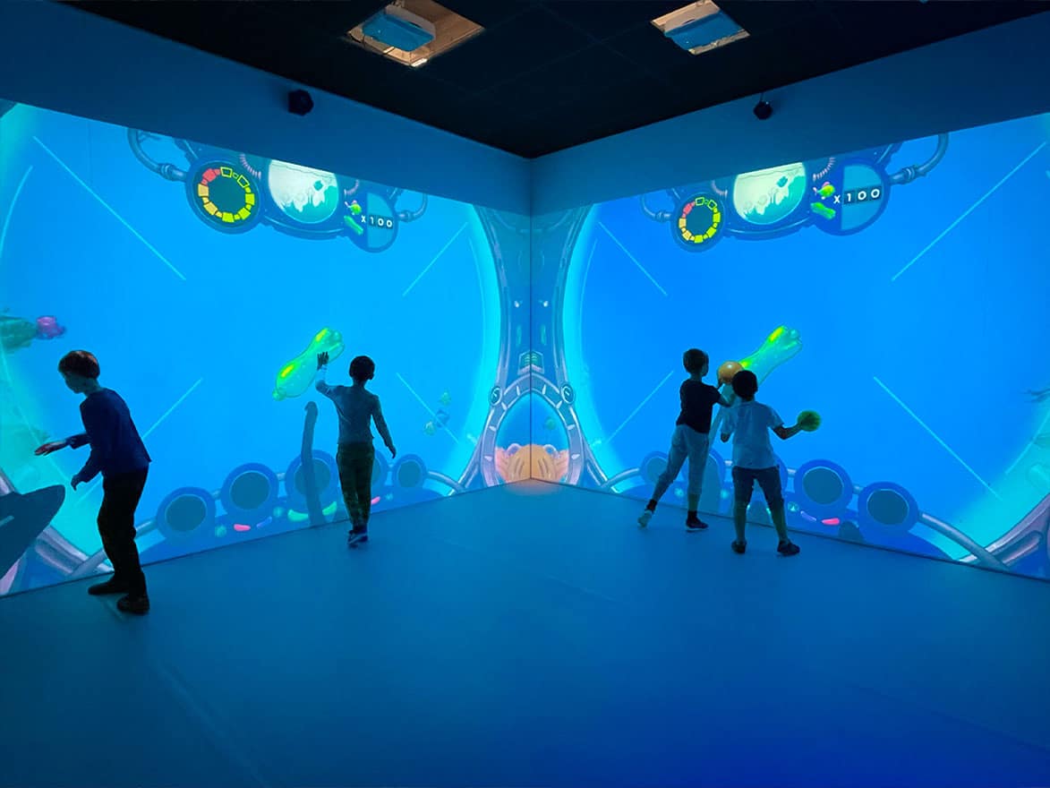 Salle immersive avec 4 enfants jouant à Clean the Ocean sur des murs interactifs