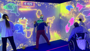 Trois personnes, dont une en fauteuil roulant, jouent sur un mur interactif dans une salle immersive inclusive