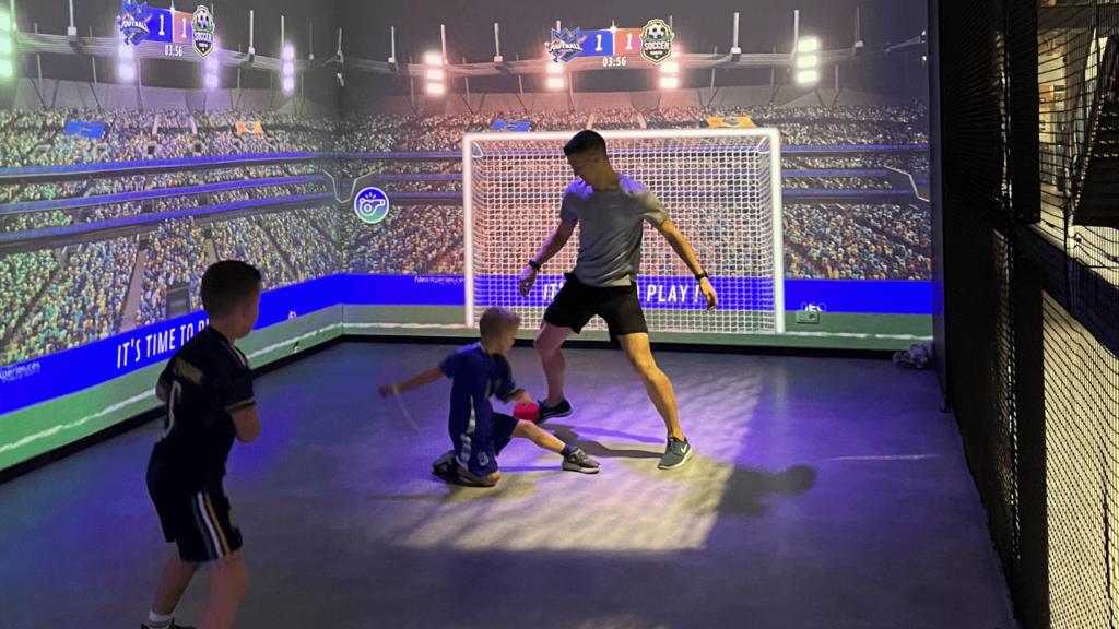 Personnes jouant au foot dans une salle immersive sur des murs interactifs