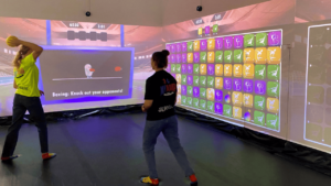 Two people playing a puzzle and sports game projected on interactive walls in an immersive room
