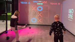 Deux personnes jouant au morpion projeté sur un mur interactif dans une salle immersive Neo-One