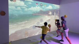 Trois enfants jouent à Break It Hand sur un mur interactif projetant une plage tropicale avec des cibles à atteindre