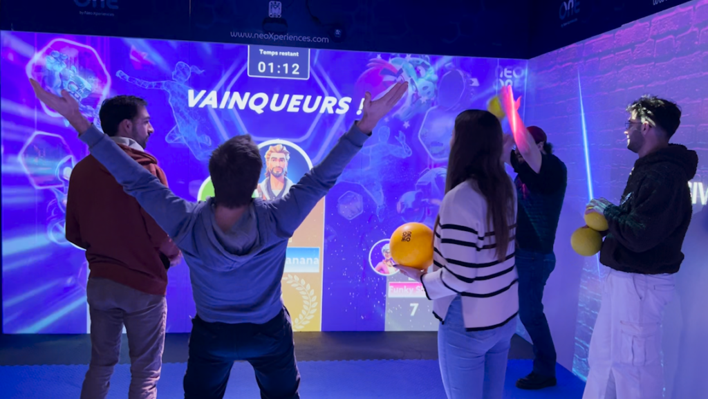 Joueurs célébrant une victoire devant un mur interactif dans une session de competitive social gaming chez NeoXperiences
