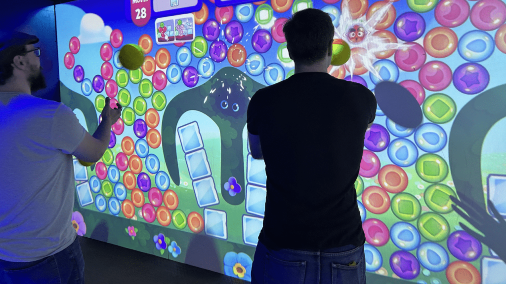 Deux adultes jouant à Angry Birds Dream Blast sur un mur interactif NeoXperiences géant et coloré