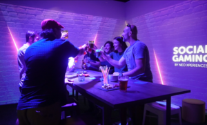 Groupe d’adultes trinquant autour d’une table dans une salle de competitive social gaming entouré de murs interactifs NeoXperiences